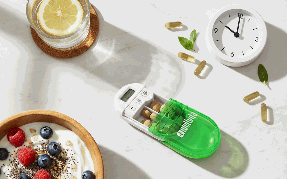 Daglig kosttilskud-rutine med pilleboks opdelt i morgen, middag og aften på marmorbord med glas vand og morgenmad