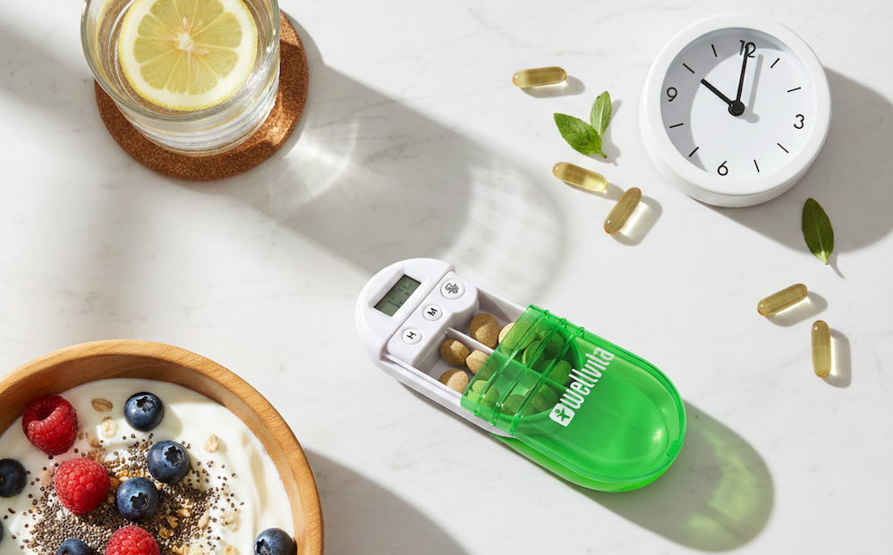 Daglig kosttilskud-rutine med pilleboks opdelt i morgen, middag og aften på marmorbord med glas vand og morgenmad